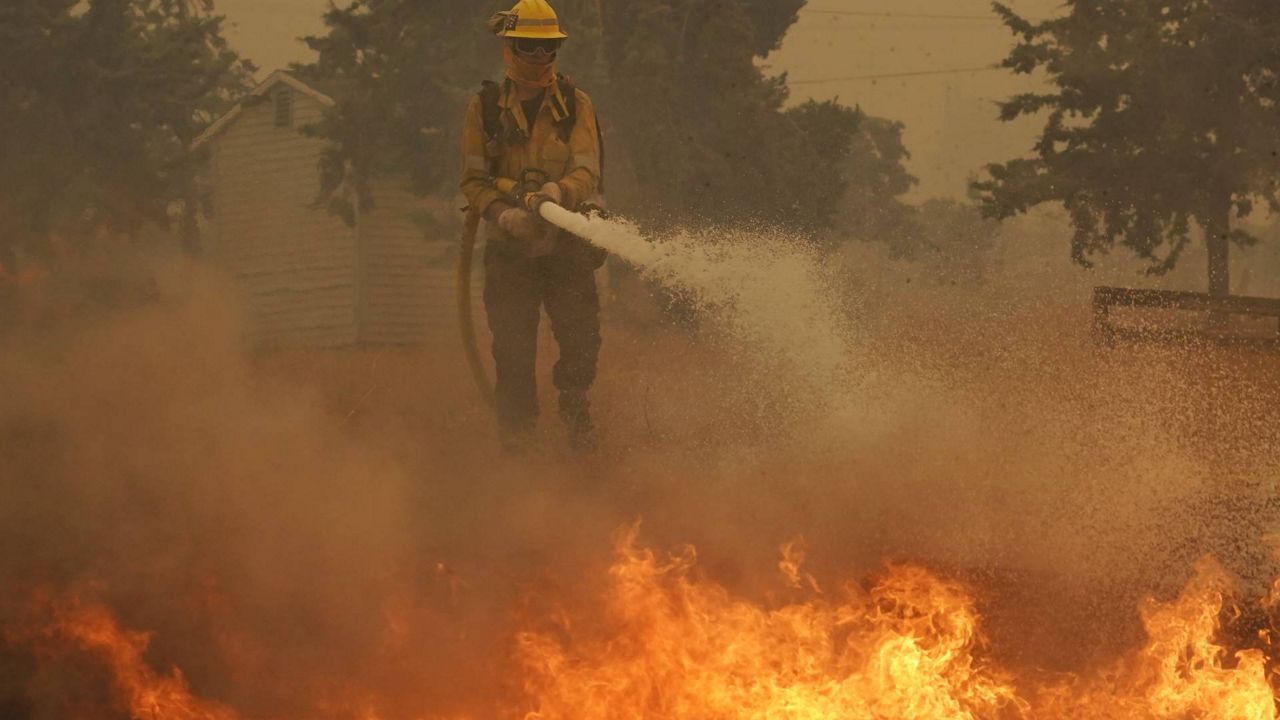 A member of a L.A. County Fire crew hoses down flames while protecting a home from the advancing Bobcat Fire along Cima Mesa Rd., Sept. 18, 2020, in Juniper Hills, Calif. (AP/Marcio Jose Sanchez)
