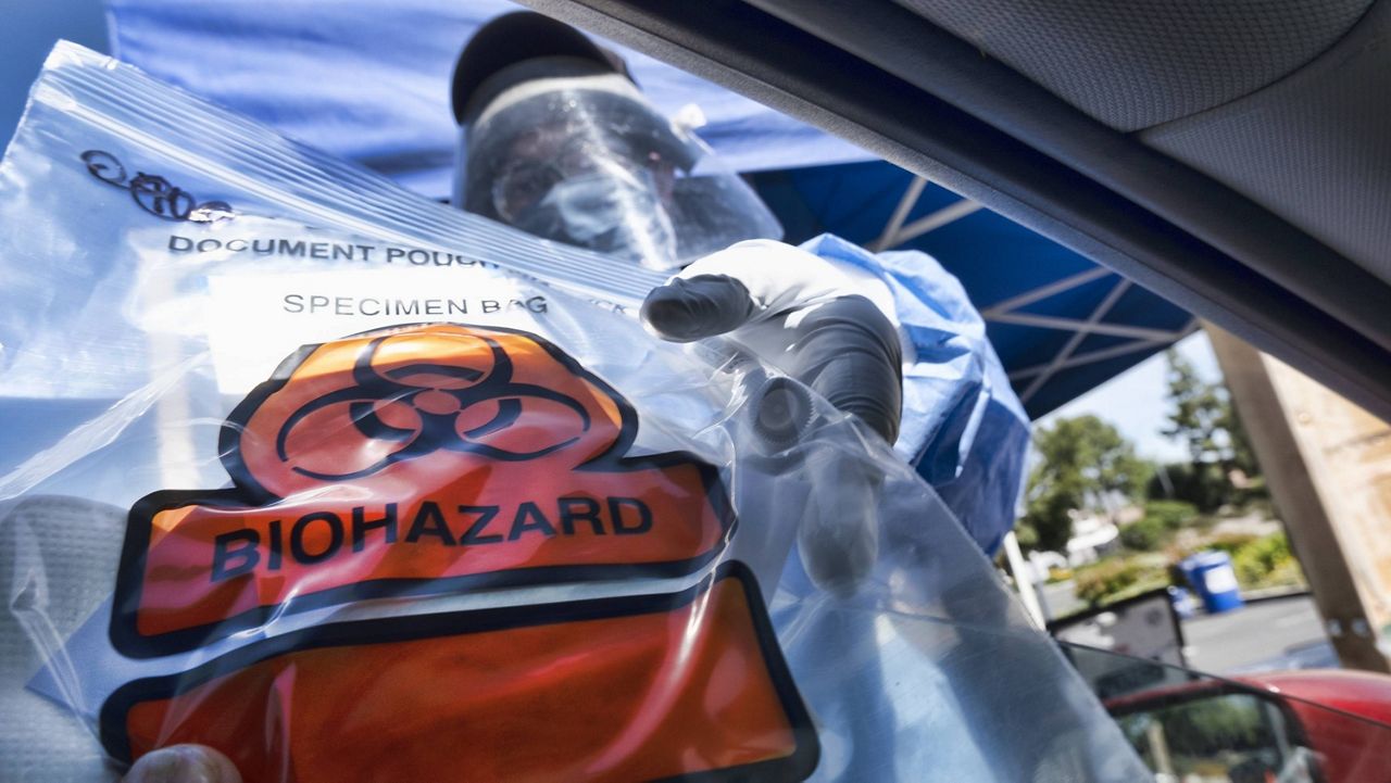 In this May 6, 2020 photo a medical worker hands a self administered coronavirus test to a patient at a drive through testing site in a parking lot in the Woodland Hills section of Los Angeles. (AP Photo/Richard Vogel, File)