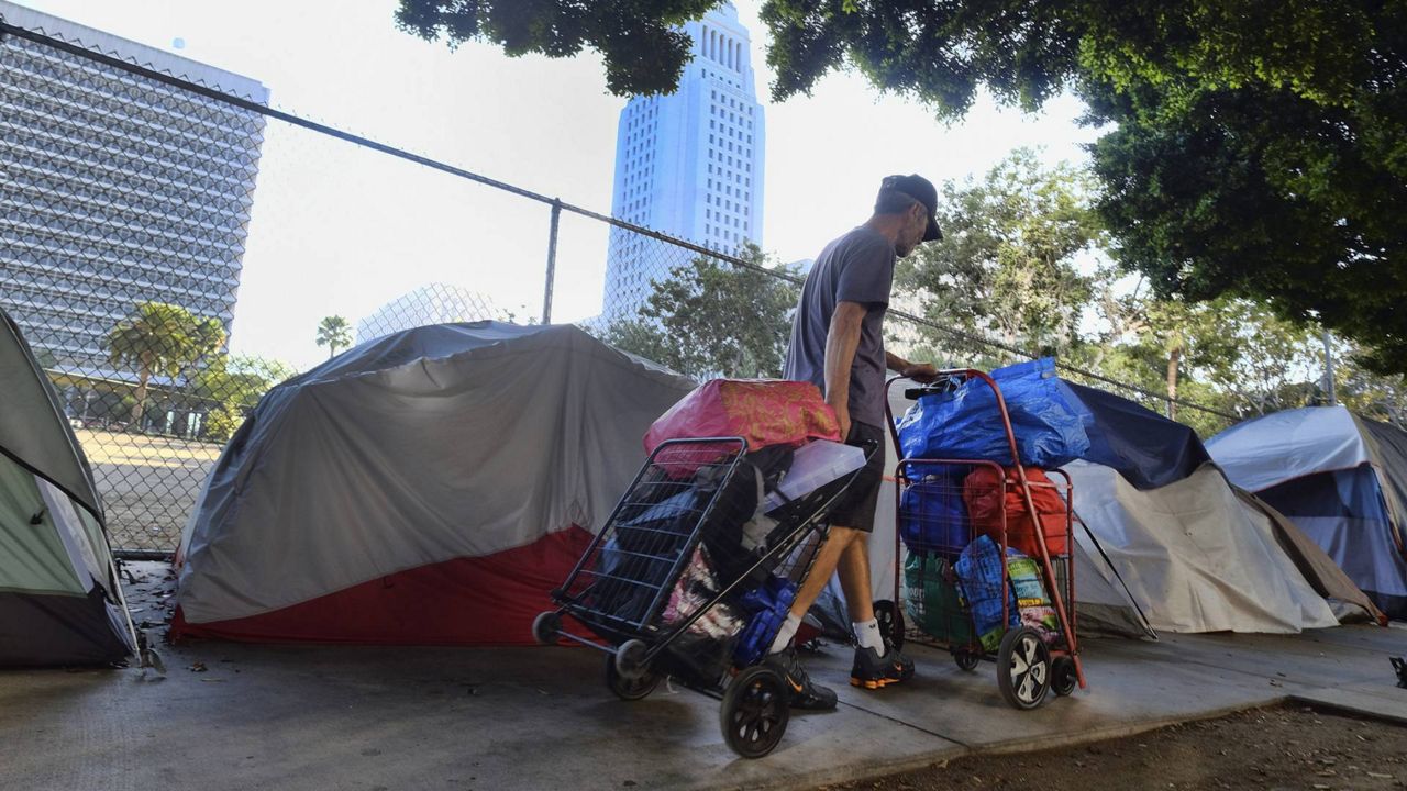 In this July 1, 2019 photo, a homeless man moves his belongings from a street behind Los Angeles City Hall as crews prepare to clean the area. (AP/Richard Vogel)