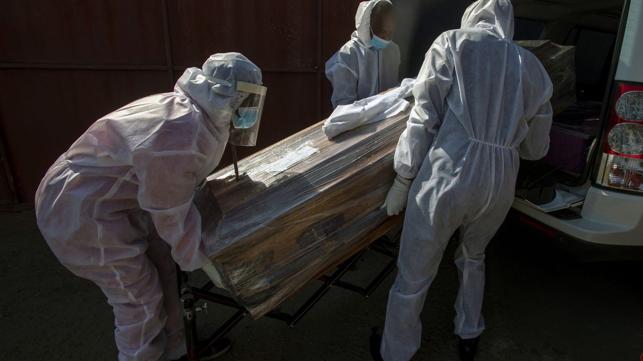 FILE - In this July 21 2020, file photo, funeral home workers in protective suits carry the coffin of a woman who died from COVID-19 into a hearse in Katlehong, near Johannesburg, South Africa. (AP Photo/Themba Hadebe, File)