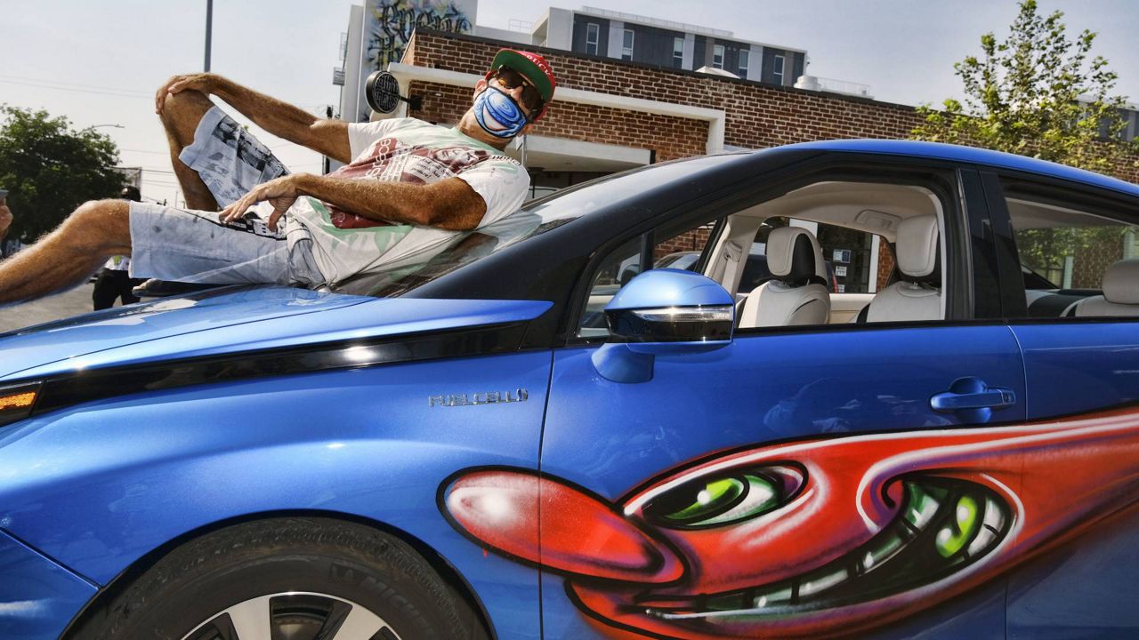 Artist Kenny Scharf poses on his car with one of his paintings during the "Karbombz!" rally of about 50 cars, all painted by Scharf, in the Hollywood section of LA, Sept. 26, 2020. (AP Photo/Richard Vogel)
