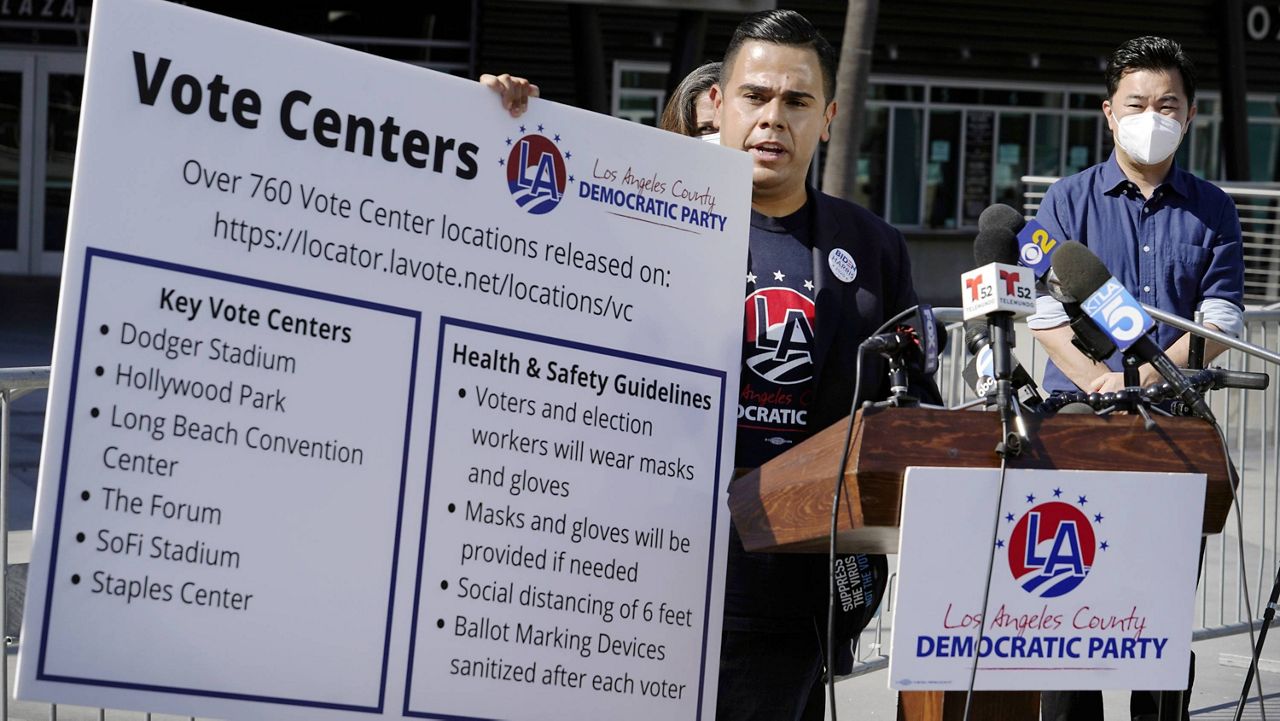 Los Angeles County Democratic Party Chair Mark J. Gonzalez, center, flanked by David Ryu Assistant Council President Pro Tempore and Councilmember District Four, right, with other various Democratic elected leaders and candidates, hold a banner with key vote center locations and social distancing instructions, during a Los Angeles County Democratic Party news conference outside the Staples Center in Los Angeles, Thursday, Oct. 1, 2020. (AP Photo/Damian Dovarganes)