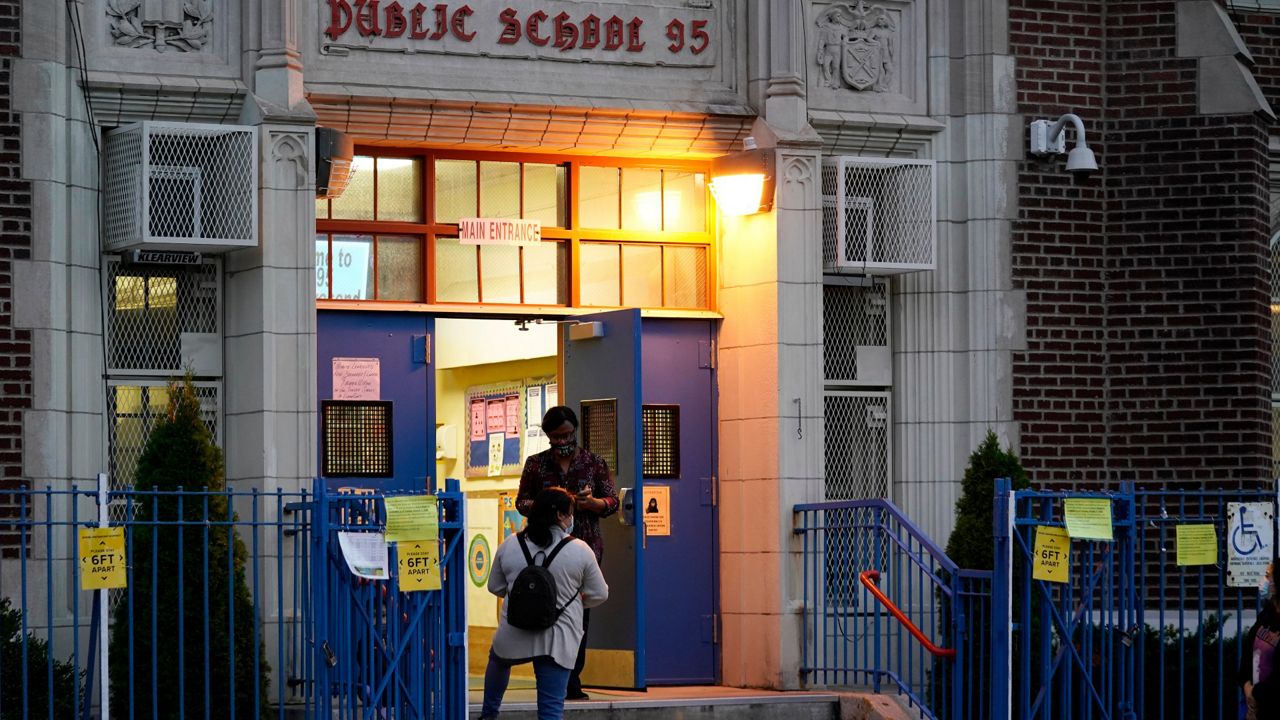 A Department of Education employee talks to a parent on the steps outside Public School 95 in Brooklyn's Gravesend neighborhood Monday, Oct. 5, 2020, in New York. 