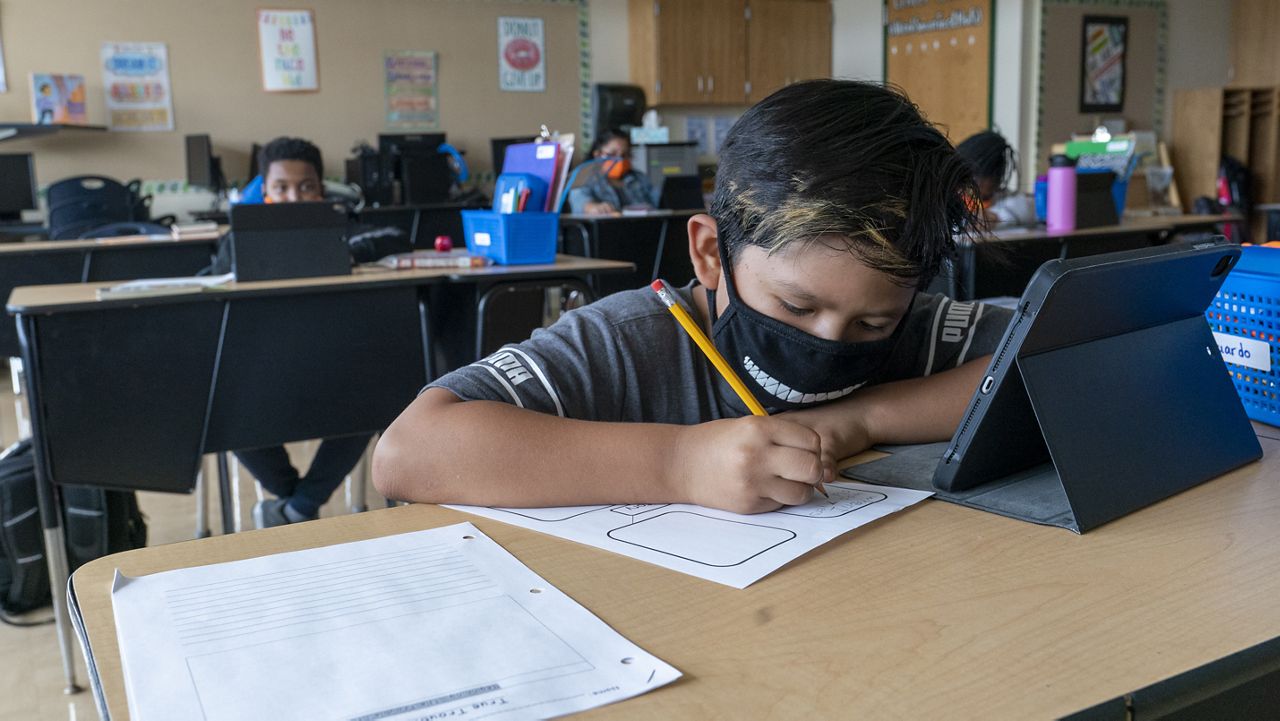 A student wears a face mask while doing work at his desk at the Post Road Elementary School, Thursday, Oct. 1, 2020, in White Plains, N.Y. (AP Photo/Mary Altaffer)