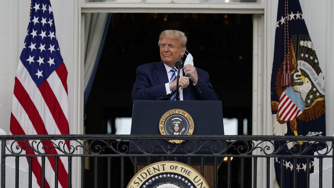 President Donald Trump removes his face mask to speak from the Blue Room Balcony of the White House to a crowd of supporters, Saturday, Oct. 10, 2020, in Washington. (AP Photo/Alex Brandon)