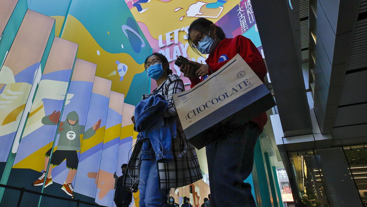 Shoppers wearing face masks to help curb the spread of the coronavirus with their purchased goods walk through the capital city's popular shopping mall in Beijing on Monday. (AP Photo/Andy Wong)