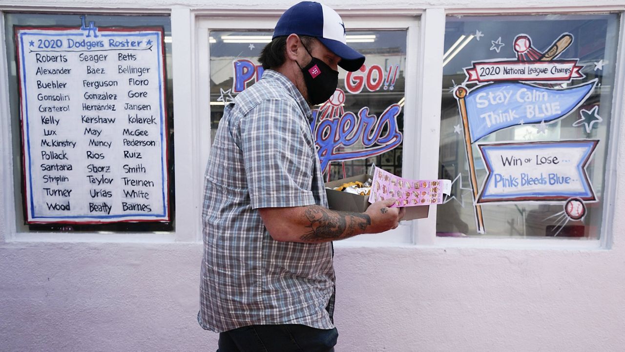 A customer carries his order outside Pink's Hot Dogs, which is decorated in Dodgers blue in support of the Los Angeles Dodgers, who are playing in the 2020 World Series against the Tampa Bay Rays Wednesday, Oct. 21, 2020, in Los Angeles. (AP Photo/Ashley Landis)