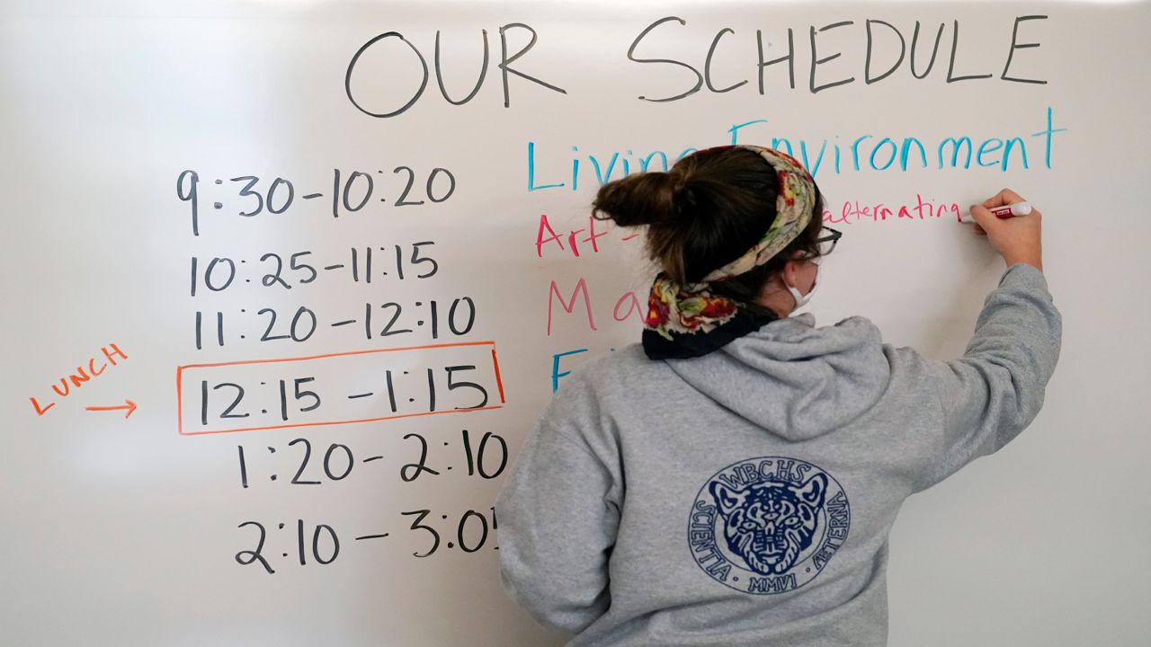 Global history teacher Alis Anasal writes the schedule on a white board in her classroom at West Brooklyn Community High School, Thursday, Oct. 29, 2020, in New York. The high school is a "transfer school," catering to students who haven't done well elsewhere, giving them a chance to graduate and succeed. The school is partnered with Good Shepherd Services, who provides advocate counselors to help students achieve their goals. The school, which recently reopened, was forced to shut down for three weeks due to a spike in coronavirus cases in the neighborhood.