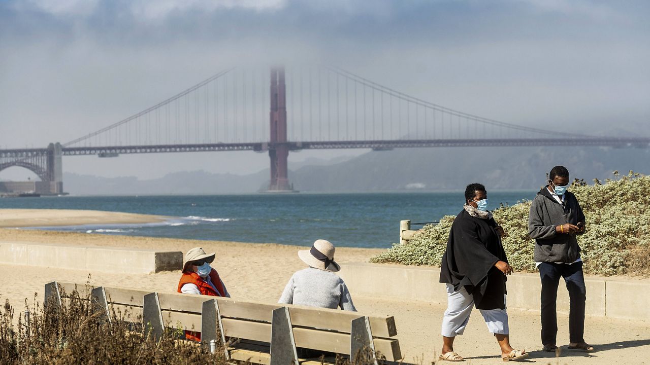 In this Oct. 22, 2020, file photo, with the Golden Gate Bridge in the background, people wear face masks while strolling at Crissy Field East Beach in San Francisco. (AP Photo/Noah Berger, File)
