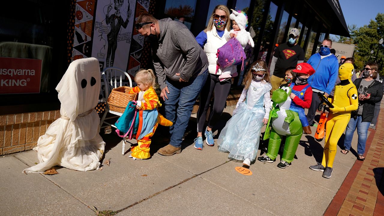 People walk past social distancing markers meant to help prevent the spread of the new coronavirus as they trick-or-treat for Halloween Saturday, Oct. 31, 2020, in downtown Overland Park, Kan. (AP Photo/Charlie Riedel)