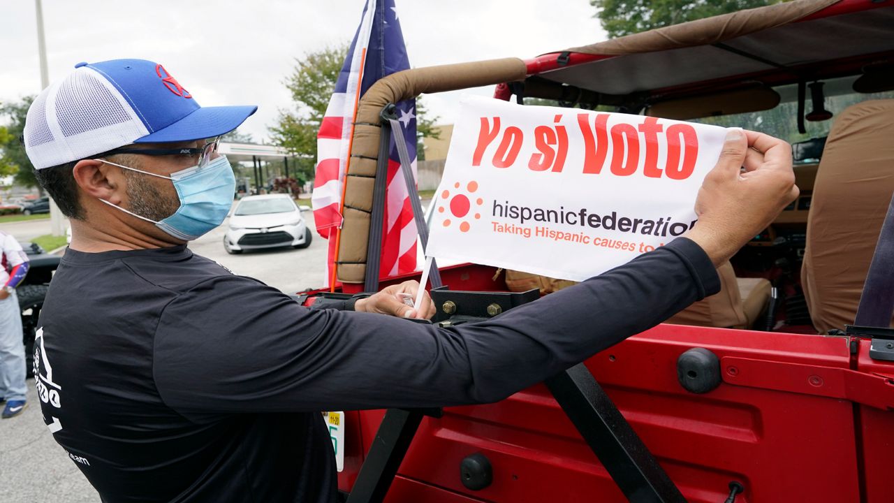 John Gimenez attaches a flag to his vehicle during an event hosted by the Hispanic Federation to encourage voting in the Latino community Sunday, Nov. 1, 2020, in Kissimmee, Fla. The Hispanic Federation is a non-partisan organization.