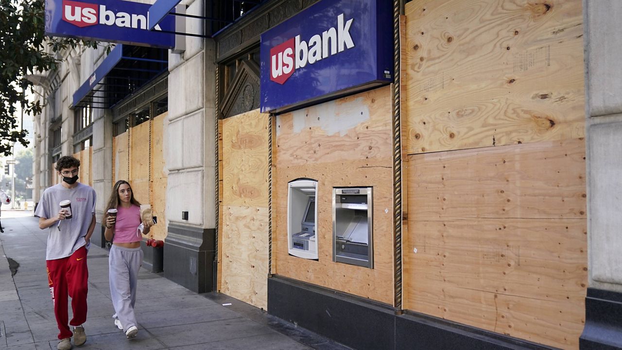 Pedestrians walk past an ATM at a boarded up US Bank branch, Monday, Nov. 2, 2020, in downtown Los Angeles. (AP Photo/Chris Pizzello)