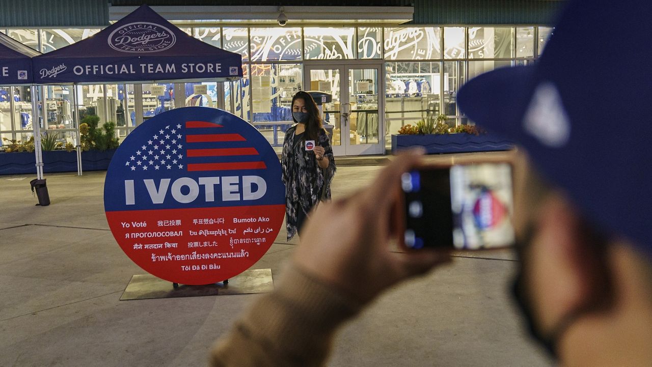 Voters take pictures with an "I Voted" sign after voting at Dodger Stadium in Los Angeles, Monday, Nov. 2, 2020. In-person voting started for most California counties this weekend as local election officials, many for the first time, opened polling places days early in hopes of avoiding crushing crowds on Election Day. (AP Photo/Damian Dovarganes)