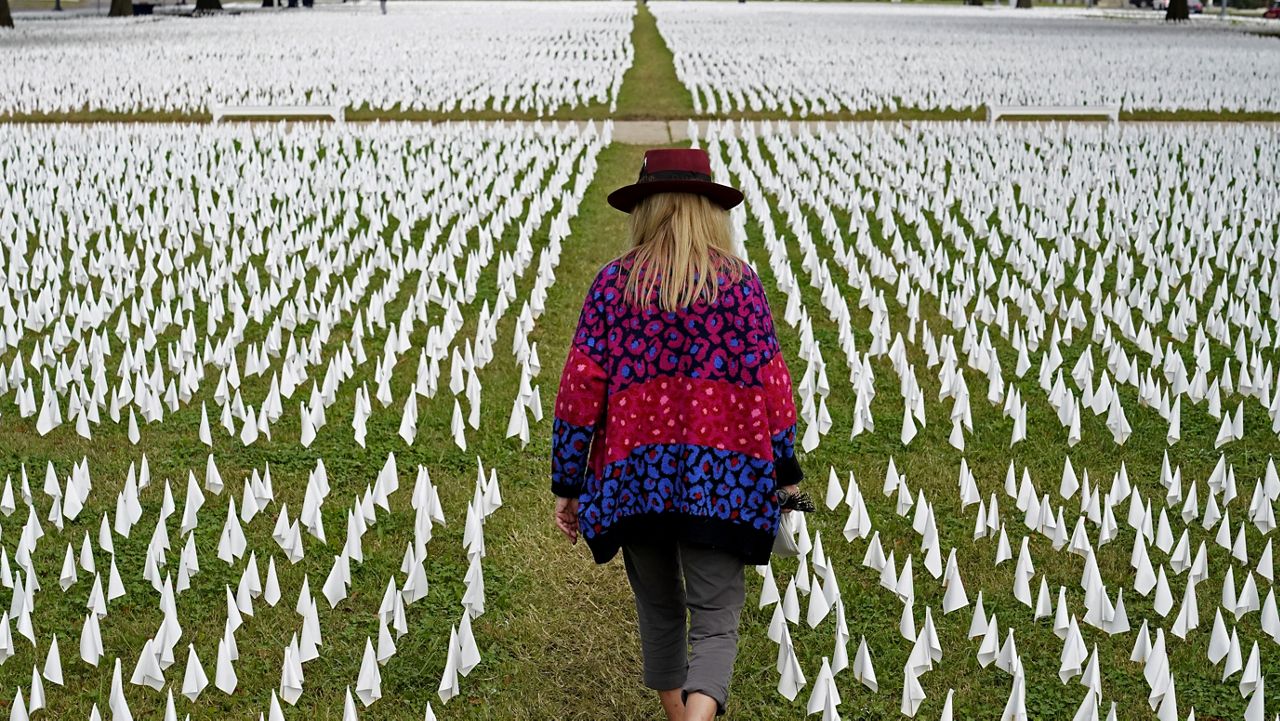 FILE - In this Oct. 27, 2020, Artist Suzanne Brennan Firstenberg walks among thousands of white flags planted in remembrance of Americans who have died of COVID-19 near Robert F. Kennedy Memorial Stadium in Washington. (AP Photo/Patrick Semansky, File)