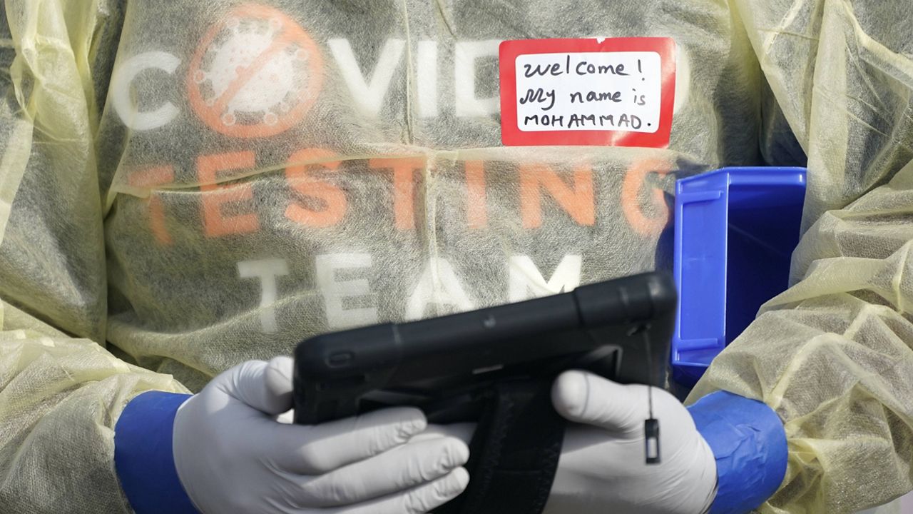 A worker wearing gloves and other PPE holds a tablet computer as he waits to check people at a King County coronavirus testing site in Auburn, Wash. (AP Photo/Ted S. Warren, File)