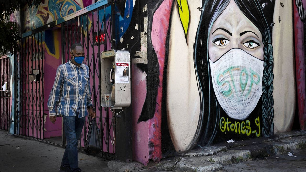 In this Oct. 1, 2020, file photo, a man wearing a face mask walks past a mural in South Central Los Angeles. (AP Photo/Jae C. Hong, File)