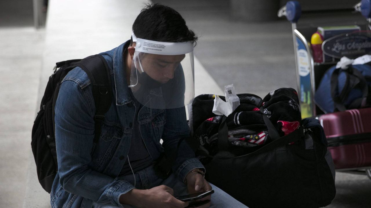 FILE - In this June 24, 2020 photo, a traveler wearing a face shield looks at his phone outside the arrivals area at Los Angeles International Airport. (AP/Jae C. Hong)