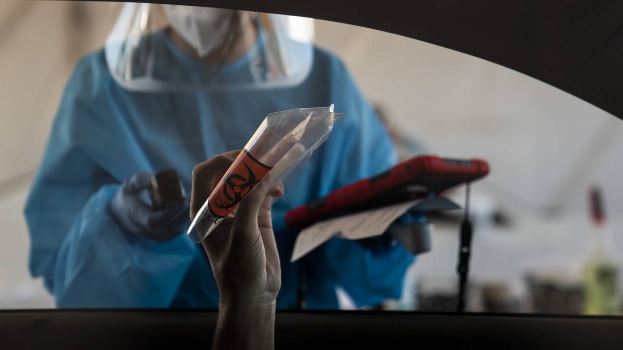 A driver holds up his nasal swab sample while talking to a medical assistant at a COVID-19 testing site set up at the OC Fairgrounds in Costa Mesa, Calif., Nov. 16, 2020. (AP/Jae C. Hong)