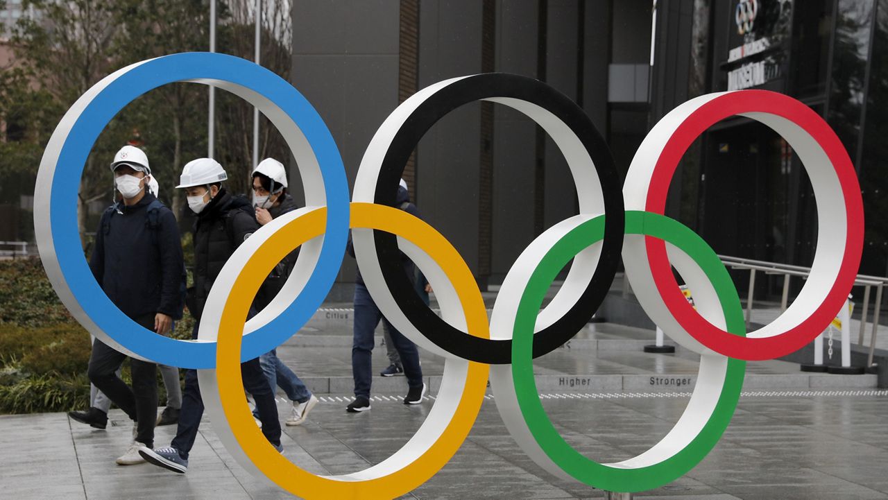 FILE - In this March 4, 2020, file photo, people wearing masks walk past the Olympic rings near the New National Stadium in Tokyo. (AP Photo/Jae C. Hong, File)