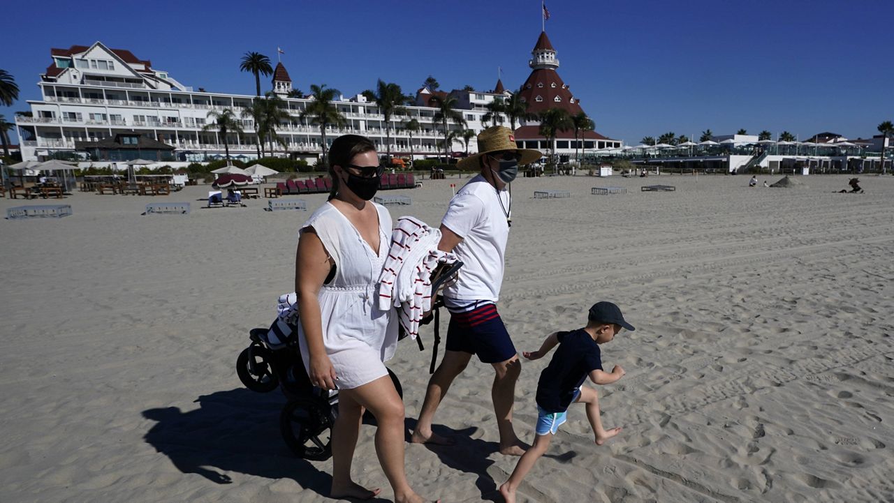 A couple wear masks as they visit the beach in front of the Hotel Del Coronado, Tuesday, Nov. 17, 2020, in Coronado, Calif. (AP Photo/Gregory Bull)