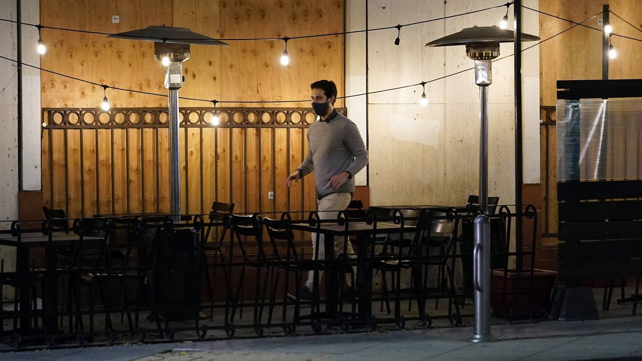 A man walks past a mostly empty outdoor seating area for a restaurant Thursday, Nov. 19, 2020, in Santa Monica, Calif. (AP Photo/Marcio Jose Sanchez)