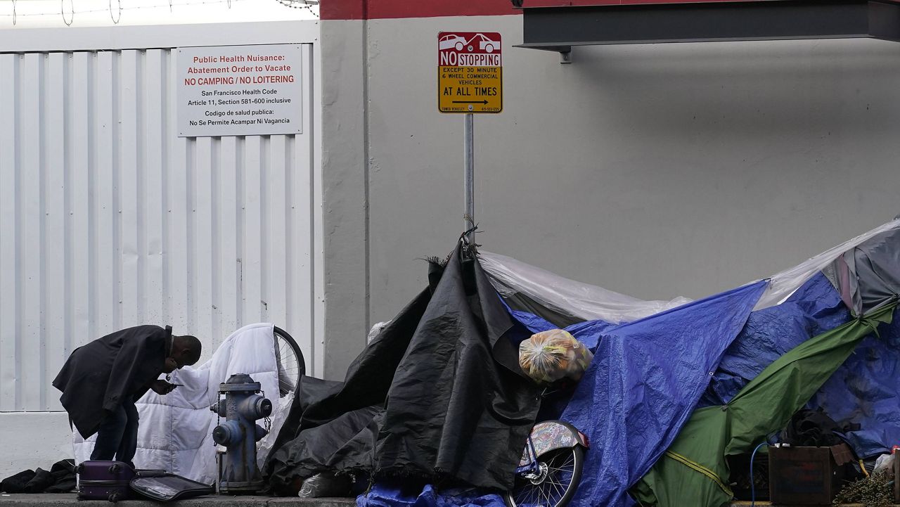 A man stands near tents set up on a sidewalk in San Francisco, Saturday, Nov. 21, 2020.  (AP Photo/Jeff Chiu)