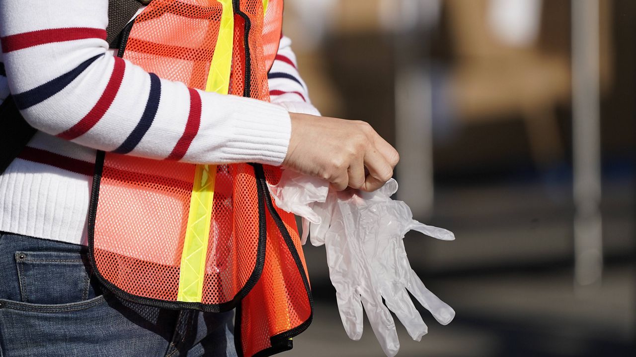 A volunteer puts on gloves after sanitizing her hands before packing boxes of food outside Second Harvest Food Bank in Thursday, Nov. 19, 2020, in Irvine, Calif. (AP Photo/Ashley Landis)