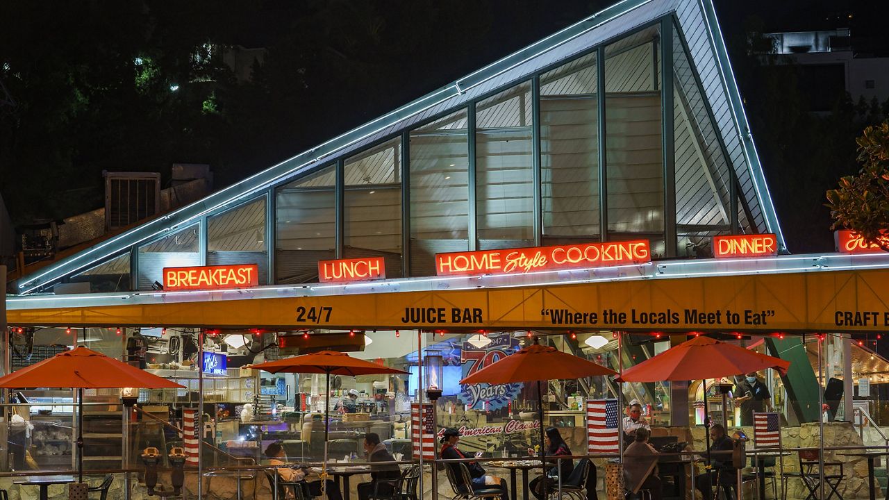Patrons sit outdoors for dinner separated by plastic dividers with flags at Mels drive-in restaurant on Sunset Boulevard on Tuesday, Nov. 24, 2020, West Hollywood, Calif. (AP Photo/Damian Dovarganes)