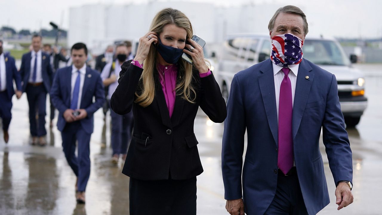 FILE- In this July 15, 2020, file photo Sen. Kelly Loeffler, R-Ga., puts on a face mask as she walks with Sen. David Perdue, R-Ga., right, at UPS Hapeville Airport Hub in Atlanta. (AP Photo/Evan Vucci, File)