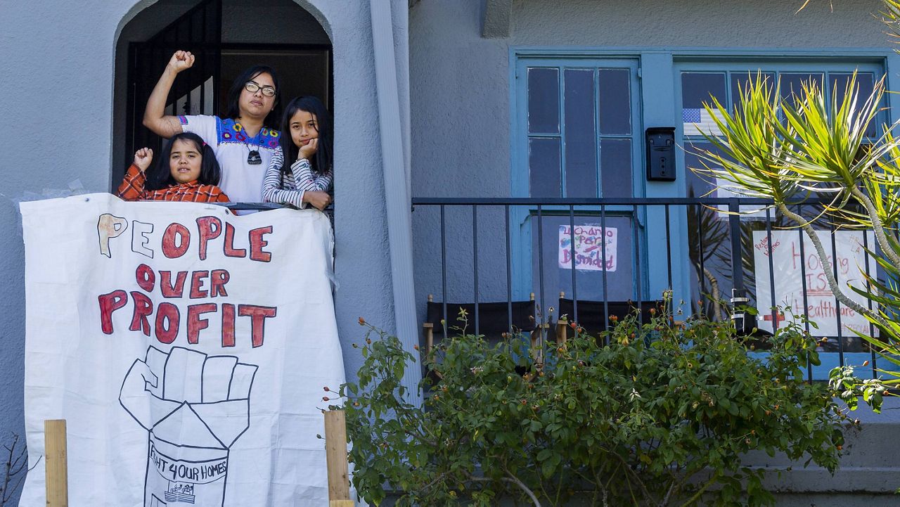In this March 30, 2020, file photo, homeless mother Martha Escudero, with her daughters, Mezcli, 8, left, and Victoria, 10, stands on the balcony outside a formerly publicly owned vacant home that her family has moved to in El Sereno neighborhood of Los Angeles. (AP Photo/Damian Dovarganes, File)