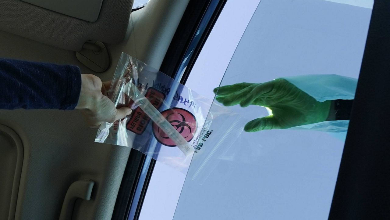 A COVID-19 test is handed through the vehicle window at a mobile testing site on Tuesday, Dec. 1, 2020, in Long Beach, Calif. (AP Photo/Ashley Landis)