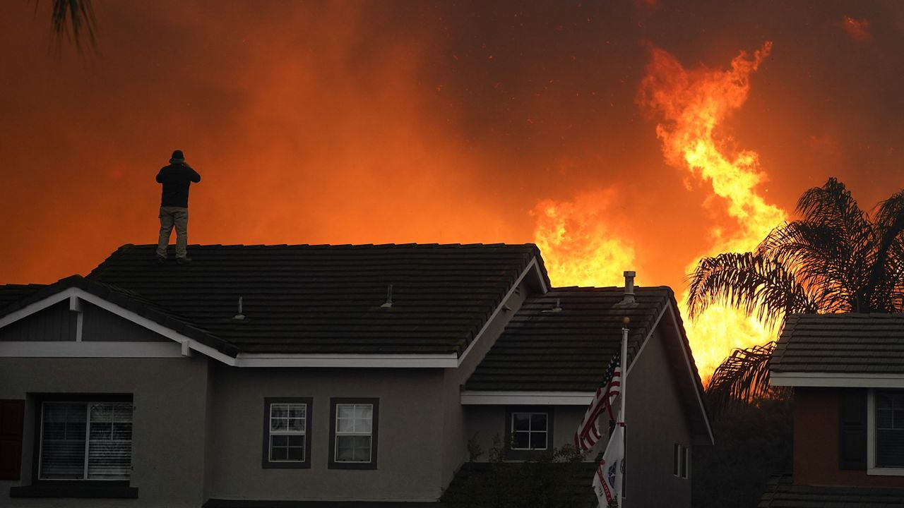 FILE - In this Tuesday, Oct. 27, 2020 file photo, Herman Termeer, 54, stands on the roof of his home as the Blue Ridge Fire burns along the hillside in Chino Hills, Calif. (AP Photo/Jae C. Hong)