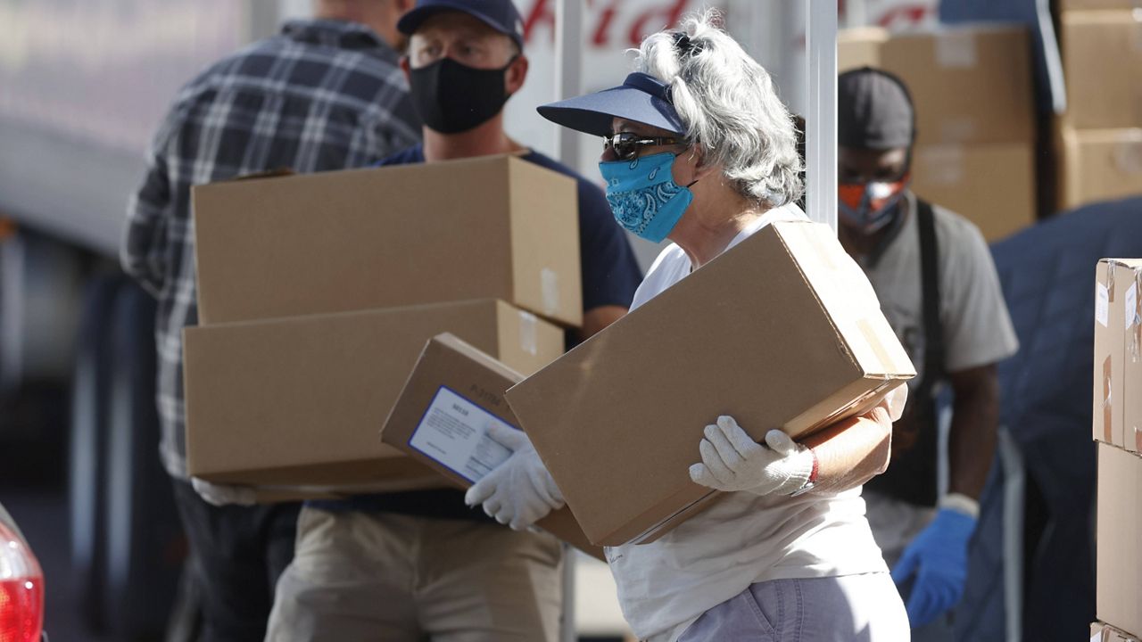 In this June 26 file photo, volunteers carry boxes of food to a waiting car at a large mobile pantry set up by the Food Bank of the Rockies in the parking lot of Empower Field at Mile High in Denver. (AP Photo/David Zalubowski, File)