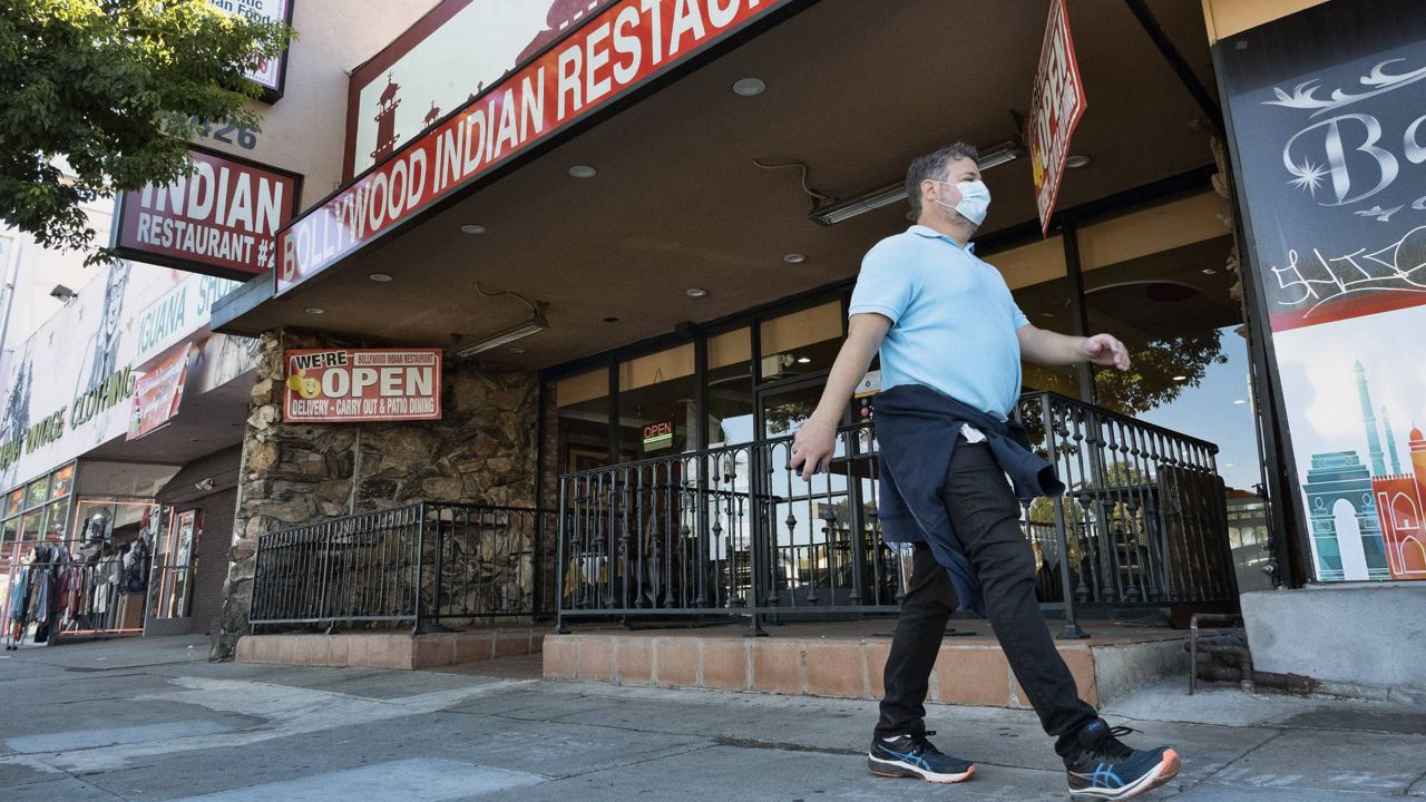 A lone masked pedestrian walks past the Bollywood Indian Restaurant open for take out in the Sherman Oaks section of Los Angeles on Dec. 6, 2020. (AP Photo/Richard Vogel)