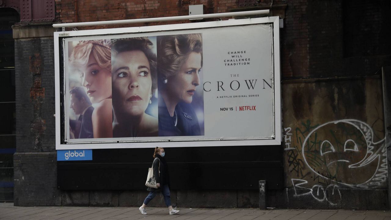 A woman wearing a face mask to curb the spread of the coronavirus walks past a billboard advertising "The Crown" TV series in central London, Monday, Dec. 7, 2020. (AP Photo/Matt Dunham)
