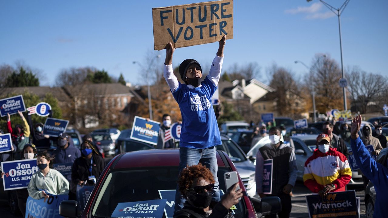 Hamilton Dickey, 8, stands on his mom's car during a rally for Democratic Georgia Senate challengers the Rev. Raphael Warnock and Jon Ossoff in Atlanta on the first day of early voting for the senate runoff Monday, Dec. 14, 2020. (AP Photo/Ben Gray)