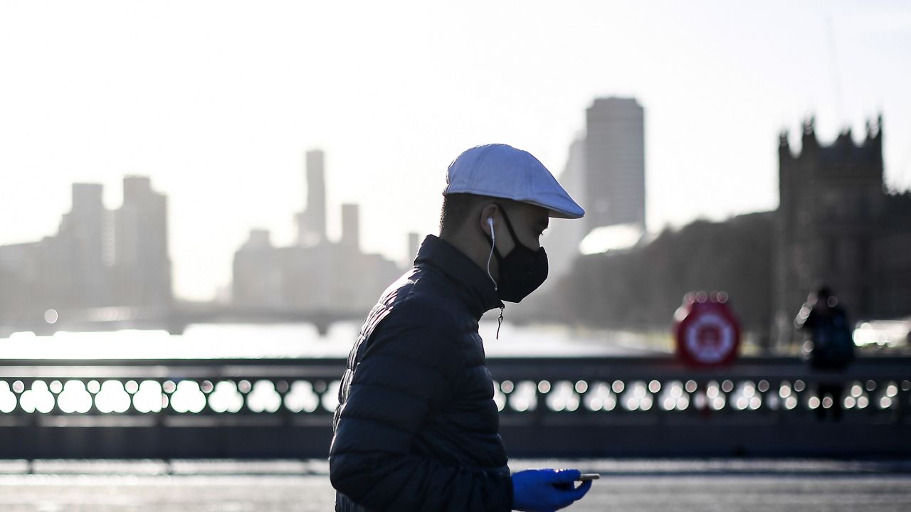 A man wears a face mask and disposable gloves as he walks on Westminster Bridge, in London, Tuesday, Dec. 15, 2020. (AP Photo/Alberto Pezzali)