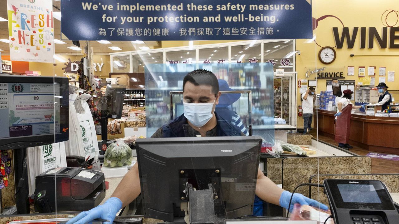 A grocery worker wears a protective mask and gloves as he helps to check out a customer from behind a plexiglass barrier at a market in the Van Nuys section of L.A. on May 5, 2020 (AP/Richard Vogel)