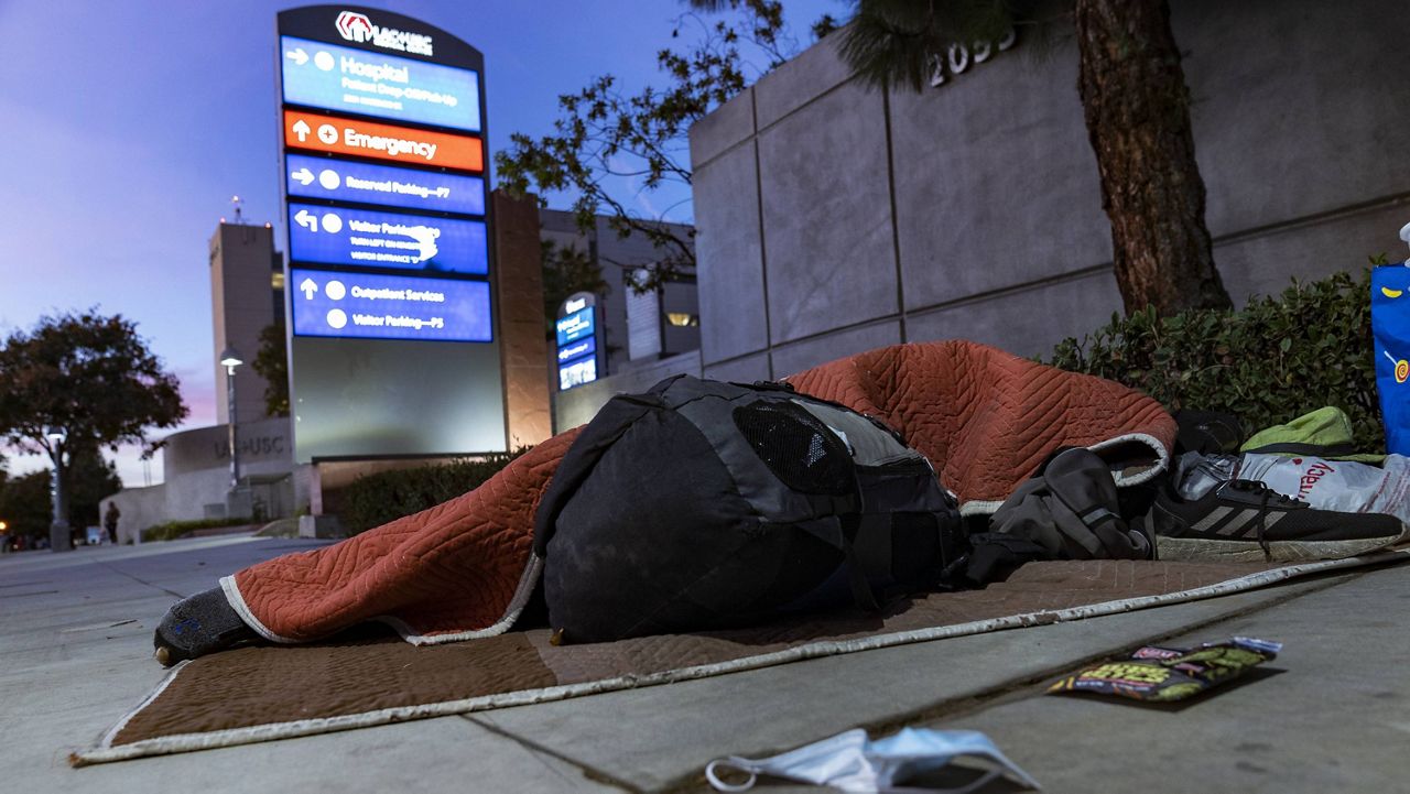 A homeless person sleeps outside the Los Angeles County+USC Medical Center hospital entrance in Los Angeles, late Wednesday, Dec. 16, 2020. (AP Photo/Damian Dovarganes)