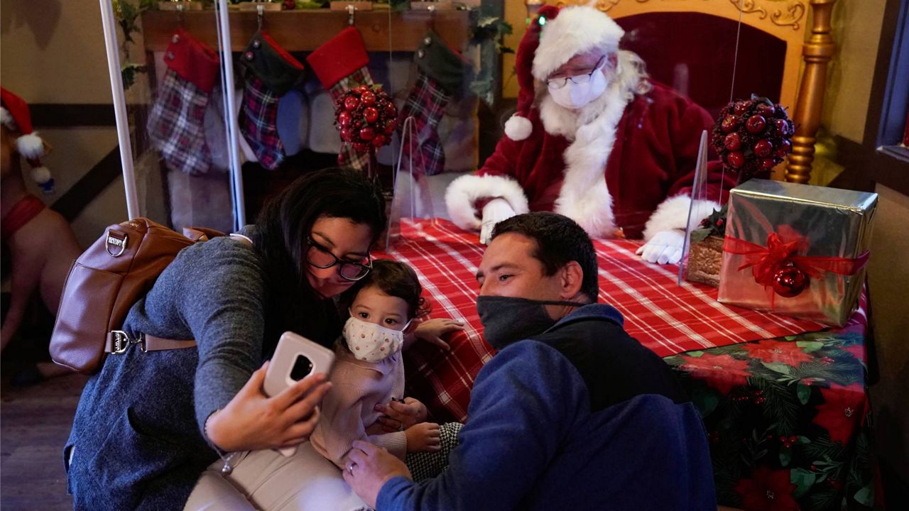 Nashua Souza, left, Sophia Souza, 2, and Kenny Souza wear face masks while taking a selfie with Ray Hamlett, who is dressed as Santa Claus, at Citadel Outlets, Dec. 4, 2020, in Los Angeles. (AP Photo/Ashley Landis)
