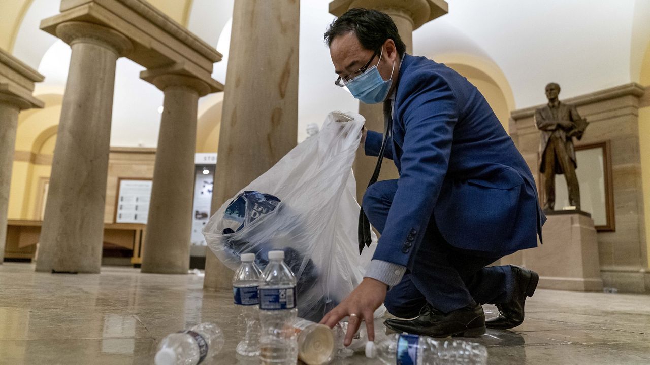 Rep. Andy Kim, D-N.J., cleans up debris and trash strewn across the floor in the early morning hours of Thursday, Jan. 7, 2021, after protesters stormed the Capitol in Washington, on Wednesday. (AP Photo/Andrew Harnik)