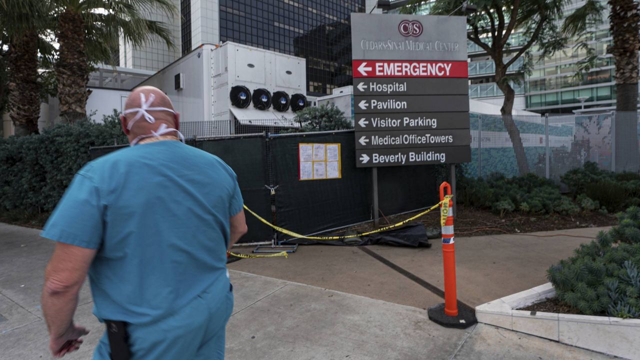 A medical worker walks past a refrigerated trailer parked outside the Cedars-Sinai Medical Center in Los Angeles Jan. 7, 2021. (AP Photo/Damian Dovarganes)