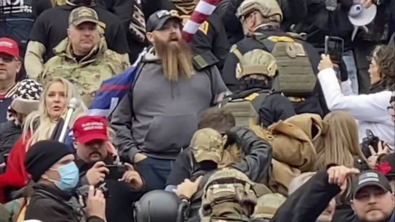 In this image from a video, a line of men wearing helmets and olive drab body armor walk up the marble stairs outside the U.S. Capitol in Washington in an orderly single-file line, each man holding the jacket collar of the man ahead. (Robyn Stevens Brody via AP)