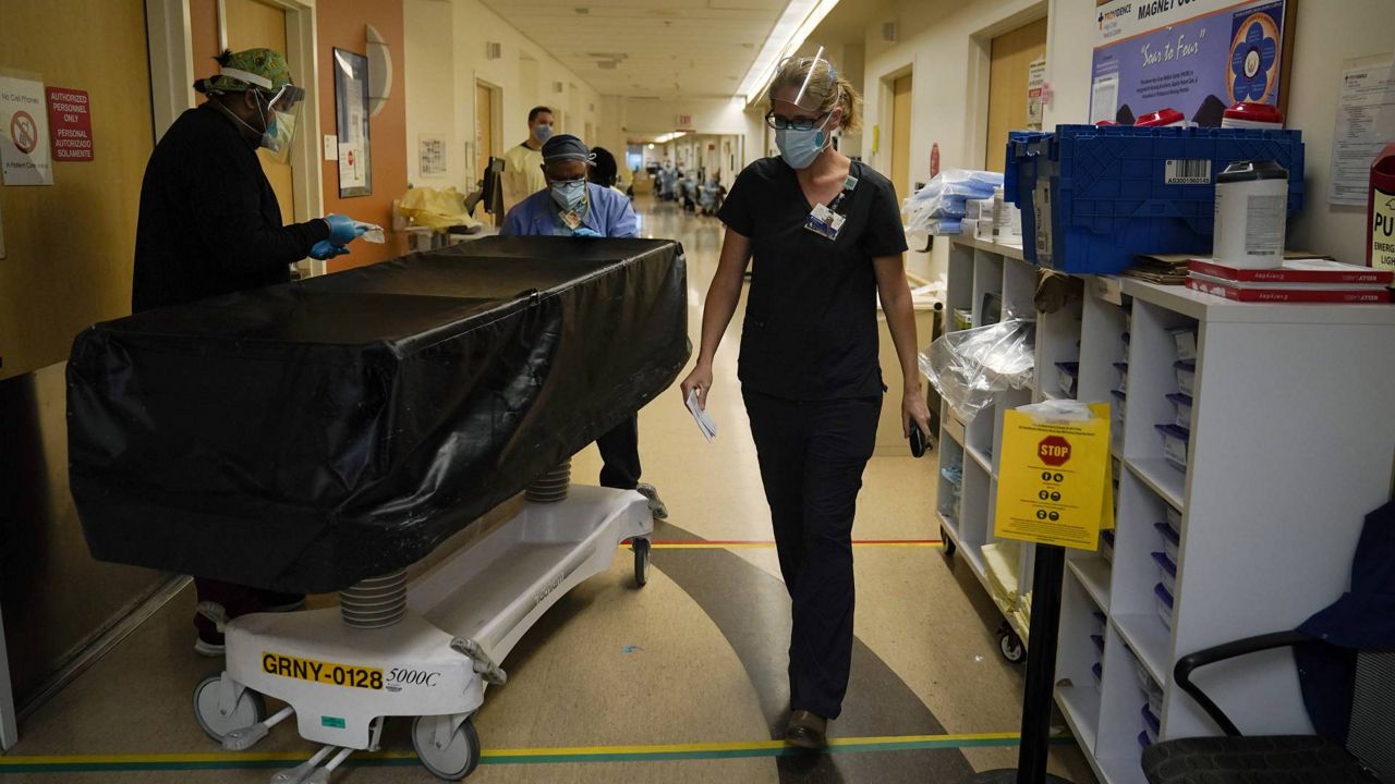 Chaplain Kristin Michealsen leaves a COVID-19 unit after talking to a family member of a deceased patient as transporters Noe Meza, left, and Miguel Lopez wheel a gurney at Providence Holy Cross Medical Center in LA on Jan. 9, 2021. (AP Photo/Jae C. Hong)