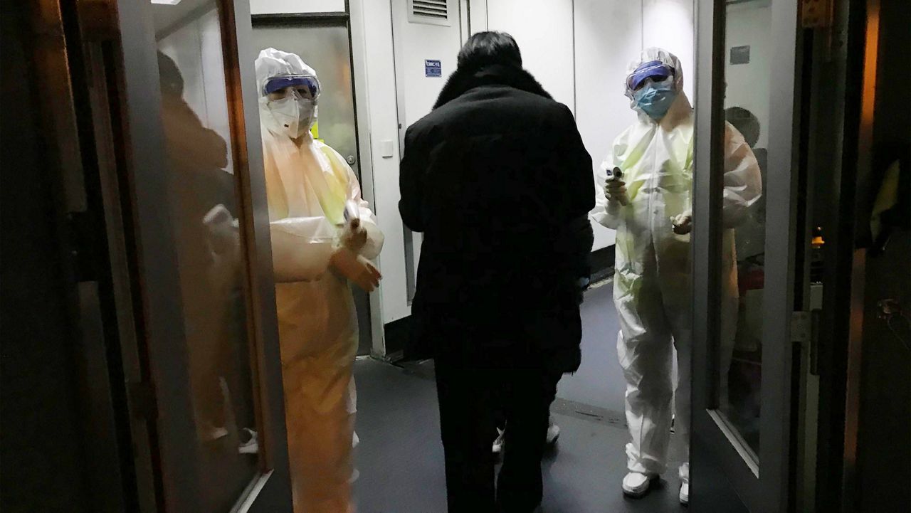 In this Jan. 22, 2020, file photo, health officials in hazmat suits wait at the gate to check body temperatures of passengers arriving from the city of Wuhan, at the airport in Beijing, China.  (AP Photo Emily Wang, File)
