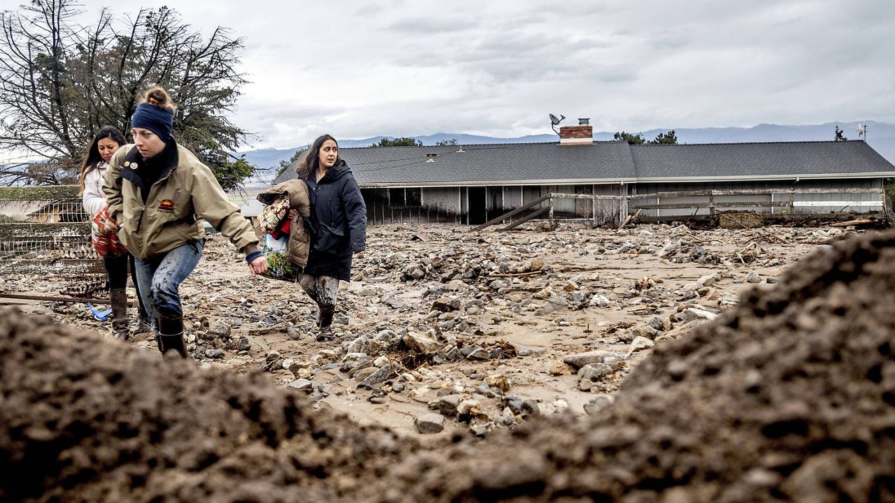 Hana Mohsin, right, carries belongings from a neighbor's home which was damaged in a mudslide on Wednesday, Jan. 27, 2021, in Salinas, Calif. (AP Photo/Noah Berger)