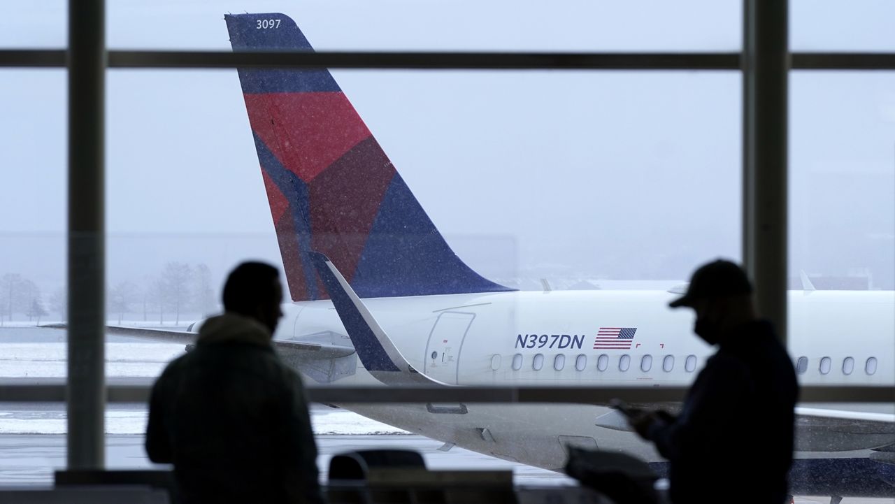 A Delta Air Lines jet sits parked at a gate as light snow falls at Ronald Reagan Washington National Airport, Tuesday, Feb. 2, 2021, in Arlington, Va. (AP Photo/Patrick Semansky)