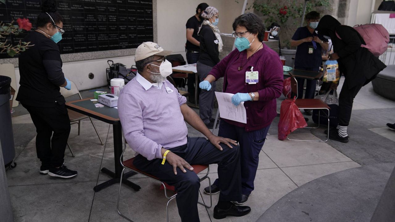 Wilbert Swaringer, a 71-year-old pastor, talks to registered nurse Julie Hurtado before getting his COVID-19 vaccine in the courtyard of the Midnight Mission in Los Angeles, Wednesday, Feb. 3, 2021. (AP/Jae C. Hong)