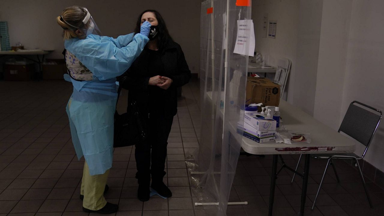 In this Dec. 27, 2020 file photo, registered nurse Leslie Clark, left, collects a nasal swab sample from a woman at a COVID-19 testing site in Los Angeles. (AP Photo/Jae C. Hong)
