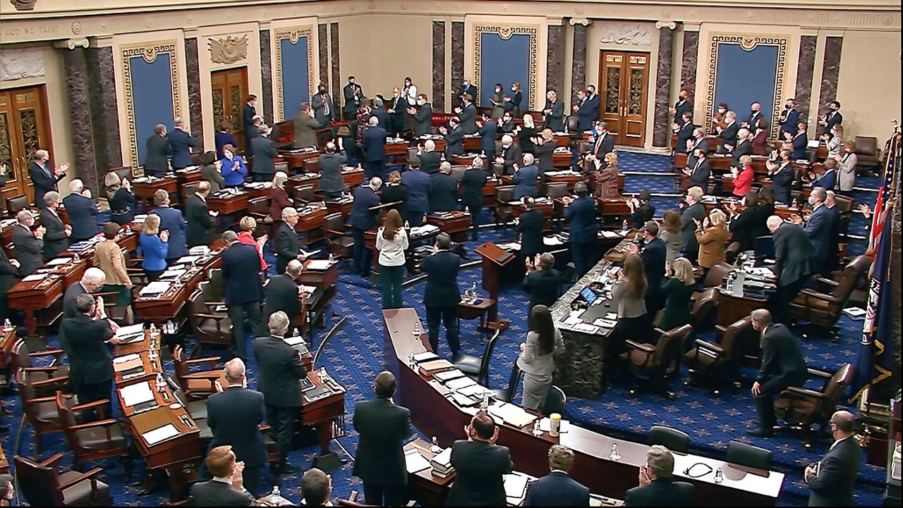 In this image from video, senators and staff give a standing ovation to U.S. Capitol Police offer Eugene Goodman, standing in the far back row with his hand over his heart, shortly before voting to award him the Congressional Gold Medal for his actions during the Jan. 6 riot. (Senate Television via AP)
